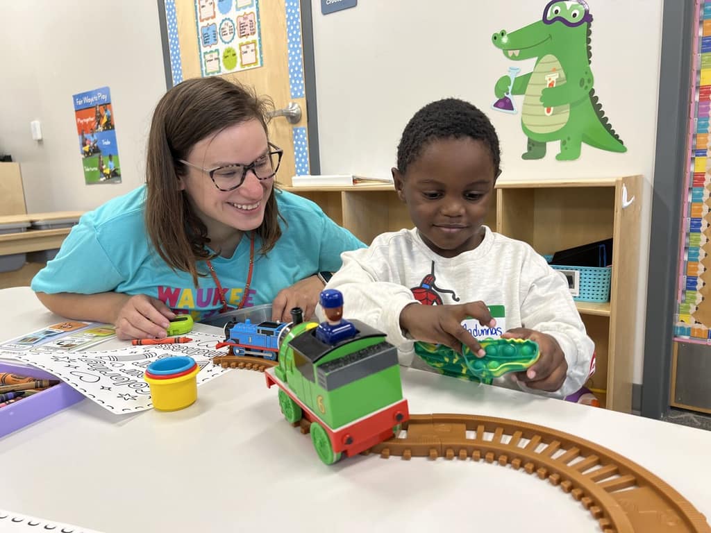 A teacher and a young student playing with a toy train